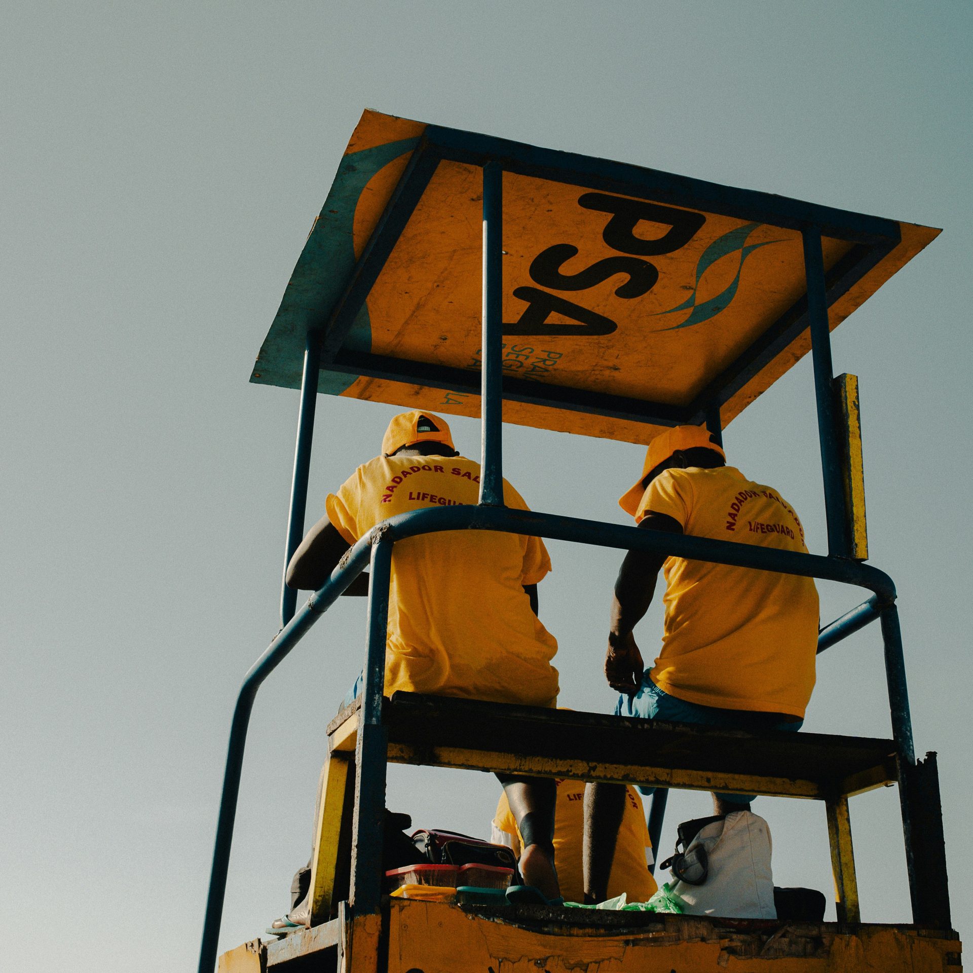 Lifeguards in yellow shirts on a tall chair.